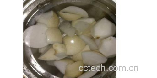 一位厨师正在厨房操作台上用清水冲洗一个金黄色的梨子,随后用削皮器去皮,并用刀将其切成均匀的块状,旁边放着一碗加了柠檬汁的清水,用于浸泡切好的梨块以防氧化 黄金梨清洗与切块过程