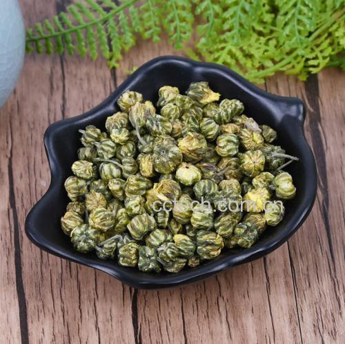 一杯清澈淡黄色的栀子野菊花茶置于木质茶几上,杯口微微冒着热气,旁边放着一朵未泡发的野菊花作为点缀,背景模糊的绿植营造出宁静养生的氛围,突出饮品的安全与自然属性 栀子野菊花茶饮成品展示图