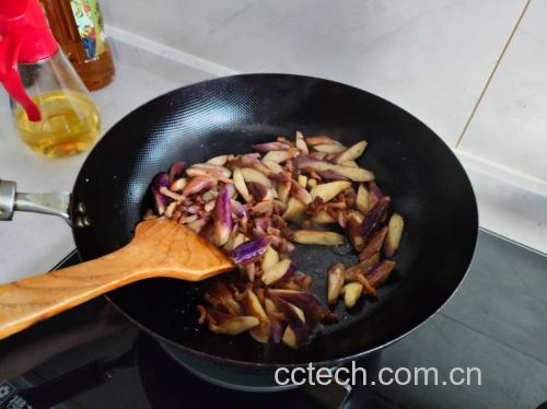 炒锅中正在炖煮茄子和扁豆角,食材已被酱汁包裹,呈现出诱人的棕红色泽,蒸汽袅袅升起,锅边可见蒜片和辣椒残留,体现家常灶台的真实感 烹饪过程图