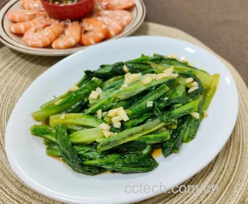 新鲜油菜被整齐地摆放在砧板上,左侧为洗净切段的油菜茎与叶分开摆放,右侧为泡洗后的淡干虾皮平铺在白色瓷碗中,背景有大蒜片和生姜丝,整体光线明亮,突出食材新鲜感 油菜与虾皮的清洗与切配过程
