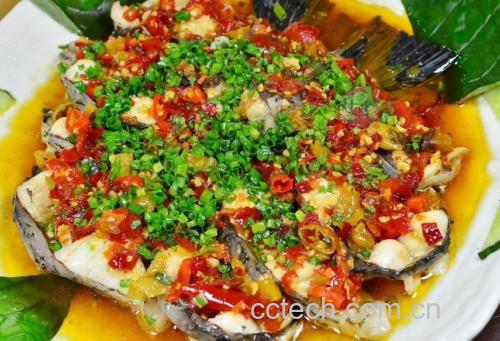 一盘红亮诱人的剁椒鱼头菜肴摆放在木质餐桌上，热气腾腾