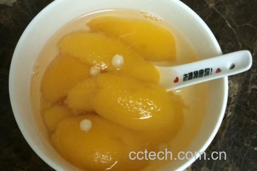 黄桃在锅中慢火炖煮，汤色呈琥珀色，周围配有冰糖、枸杞等辅料
