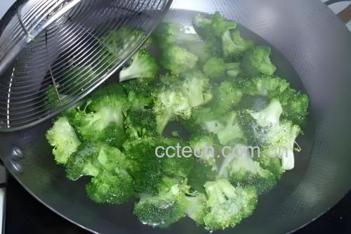 炒制过程:锅中西兰花与杏鲍菇正在翻炒,酱汁明亮,蒜片清晰可见,灶台为现代厨房环境