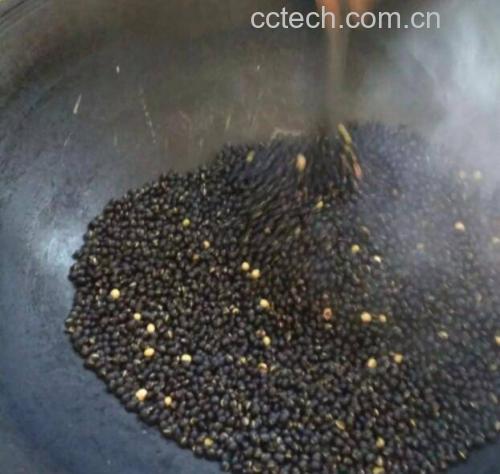 炒锅中正在翻炒黑色豆粒的特写镜头,豆子表面微泛油光,有轻微烟气上升,背景为厨房灶台环境