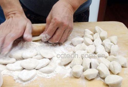 一位家庭主妇正在案板上熟练地擀制饺子皮,左手转动面剂,右手持擀面杖,动作流畅
