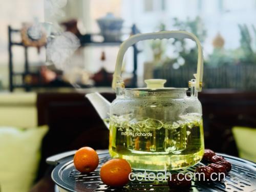 一位中老年人正在厨房用玻璃壶煮柿子树叶水