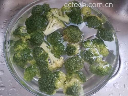 厨师正在将焯好的西兰花投入冰水中冷却，旁边摆放着切好的梨条浸泡在透明玻璃碗中