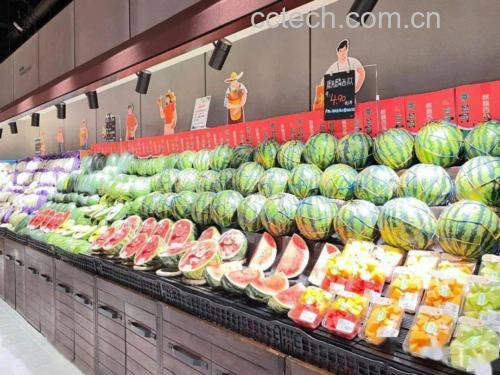 超市水果区陈列整齐的多个品种西瓜,包括圆形红瓤、椭圆形黄瓤、无籽品种等,顾客正在挑选