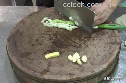 一位厨师正在用刀切新鲜大葱,案板上有葱段、葱花和完整的葱身,背景为现代厨房环境,炉灶上正在翻炒蔬菜