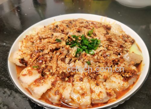 一盘红油亮泽的蒜泥白肉摆放在青瓷盘中，旁边配有蘸碟与筷子