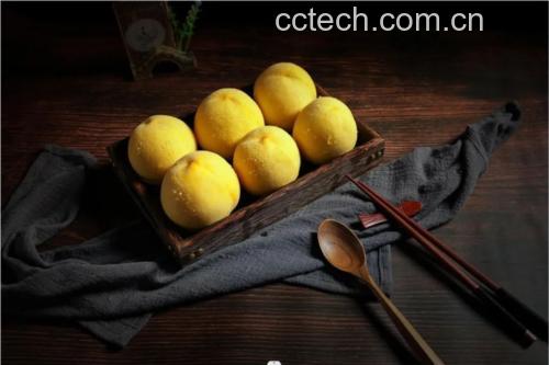 厨房操作台上摆放着刚制作完成的低糖果酱瓶,背景中有去核切块的炎陵黄桃、玻璃罐、木勺和柠檬片,旁边放着手写标签“自制炎陵黄桃低糖果酱”