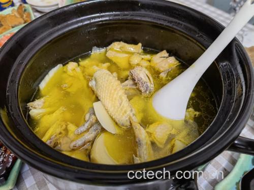 砂锅中小火慢炖的咸鸡腿，汤汁微沸，大葱段清晰可见